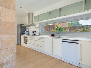 Eine moderne Küche mit weißen Schränken, einem eingebauten Backofen, einer Mikrowelle, einer Kaffeemaschine und einem Geschirrspüler.