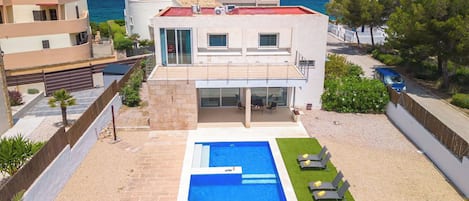 Een modern huis met twee verdiepingen, een zwembad, een overdekt terras en uitzicht op zee.