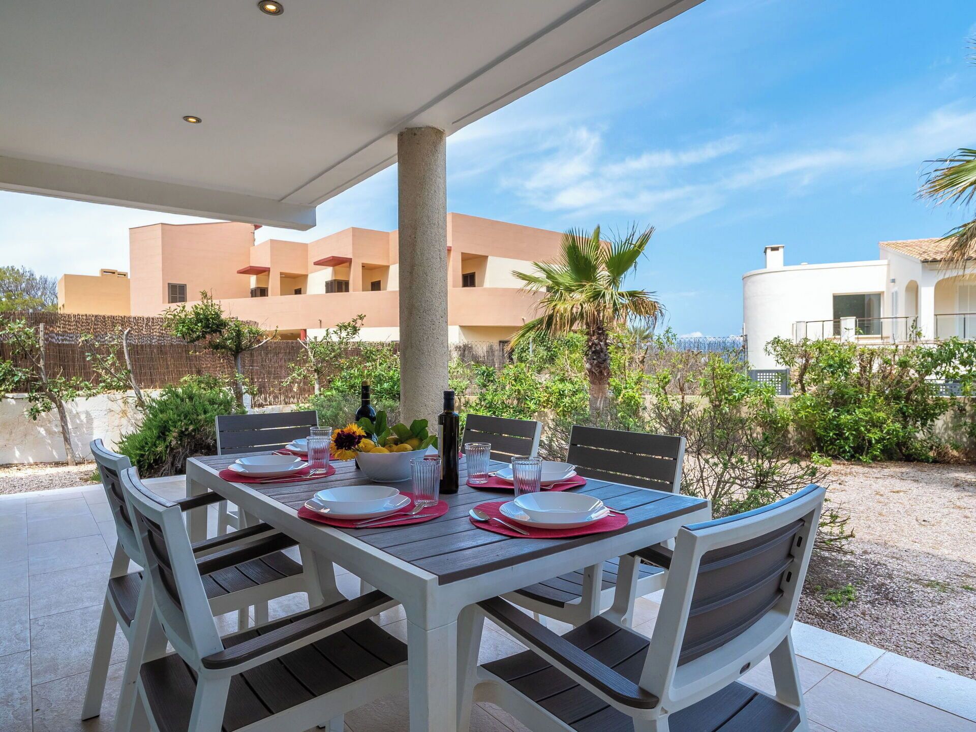 Un área de comedor al aire libre con una mesa preparada para cuatro personas, rodeada de sillas, bajo un porche cubierto.