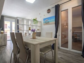 Ein Essbereich mit einem Holztisch und Stühlen, einer weißen Regaleinheit mit Dekoration und Blick ins Freie durch eine Glastür.