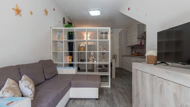 Uma sala de estar moderna com um sofá sectional cinza, uma estante branca e uma televisão de tela plana sobre um aparador de madeira.