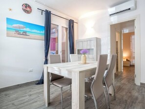 Ein Essbereich mit einem Holztisch, vier Stühlen, einer Vase mit Blumen, einer Wanduhr und einem Gemälde mit Strandmotiv.