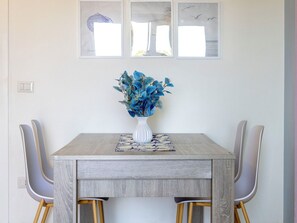 Une table à manger ornée d’un vase de fleurs bleues, deux chaises et un interrupteur fixé au mur.