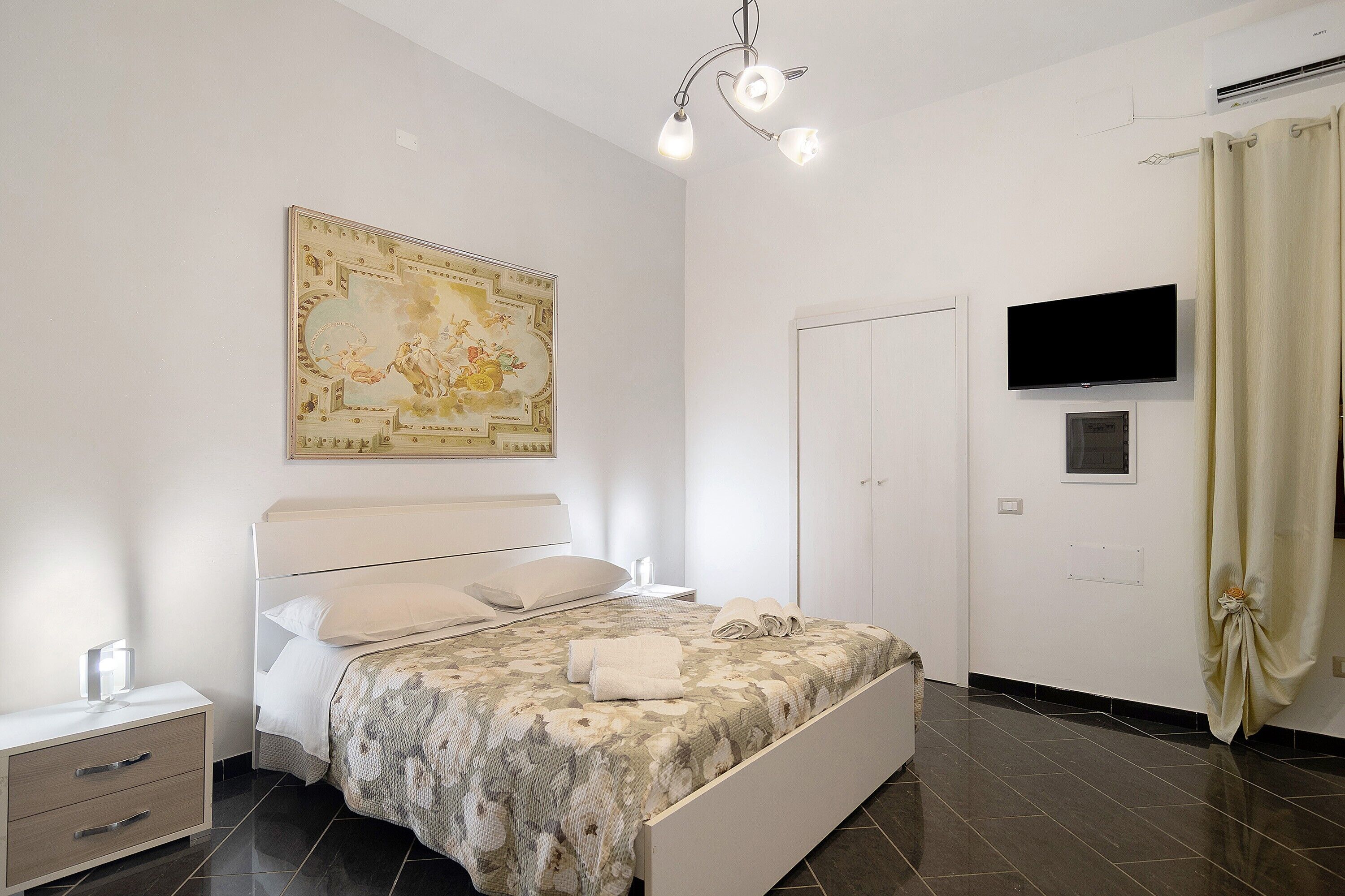 A bedroom with a bed, a nightstand, a television, and a wall-mounted air conditioner.