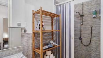Un baño con un estante de madera que contiene artículos de aseo, una ducha con cabezal de ducha manual y un inodoro.