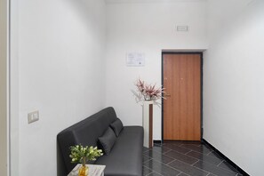 A hallway with a dark grey sofa, a white vase with flowers, and a wooden door.