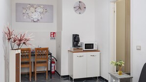 Una piccola cucina accessoriata con forno a microonde, macchina del caffè e estintore. Si trova un tavolo da pranzo con sedie e una pianta decorativa.