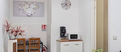 A small kitchenette with a microwave, coffee maker, and a fire extinguisher. There is a dining table with chairs and a decorative plant.