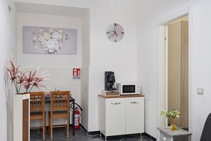 A small kitchenette with a microwave, coffee maker, and a fire extinguisher. There is a dining table with chairs and a decorative plant.