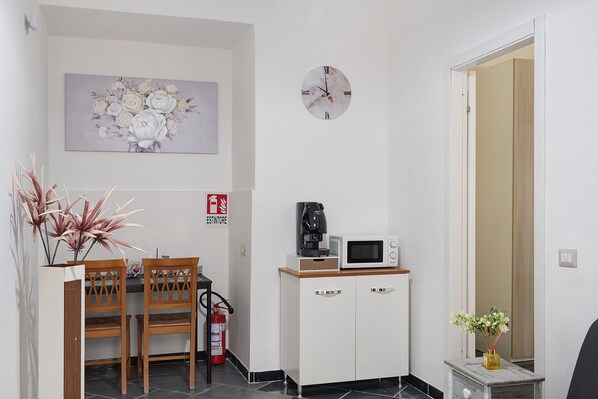 A small kitchenette with a microwave, coffee maker, and a fire extinguisher. There is a dining table with chairs and a decorative plant.