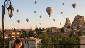 A person enjoying a meal on a balcony overlooking a cityscape with hot air balloons in the distance. - Uçhisar Palace in Cappadocia Hotel (Nevsehir)