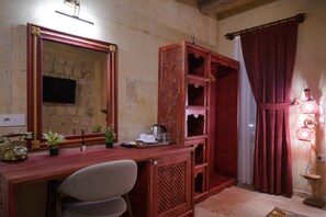 Una habitación con un escritorio de madera, una silla, un espejo, un aparador con detalles decorativos, una cortina roja y una lámpara fijada a la pared.