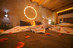 Habitación de hotel con una cama decorada con pétalos de rosa, una lámpara circular en la pared y un teléfono en la mesita de noche.