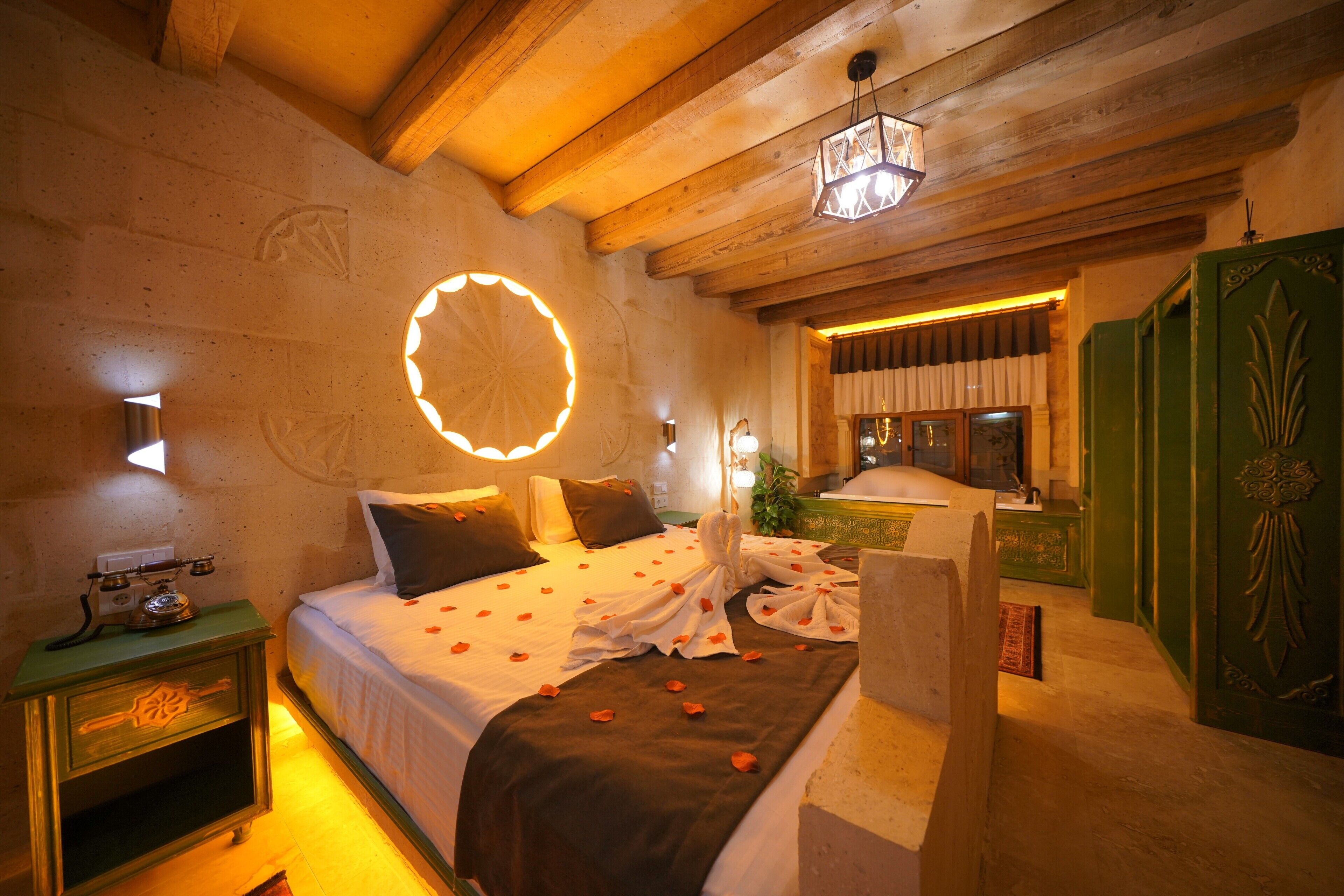 Habitación de hotel con cama, teléfono en la mesita de noche, lámpara de pared y un mueble verde con detalles decorativos tallados.