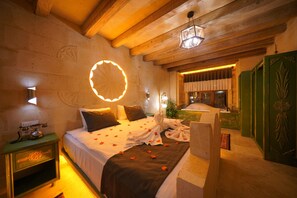 Habitación de hotel con cama, teléfono en la mesita de noche, lámpara de pared y un mueble verde con detalles decorativos tallados.