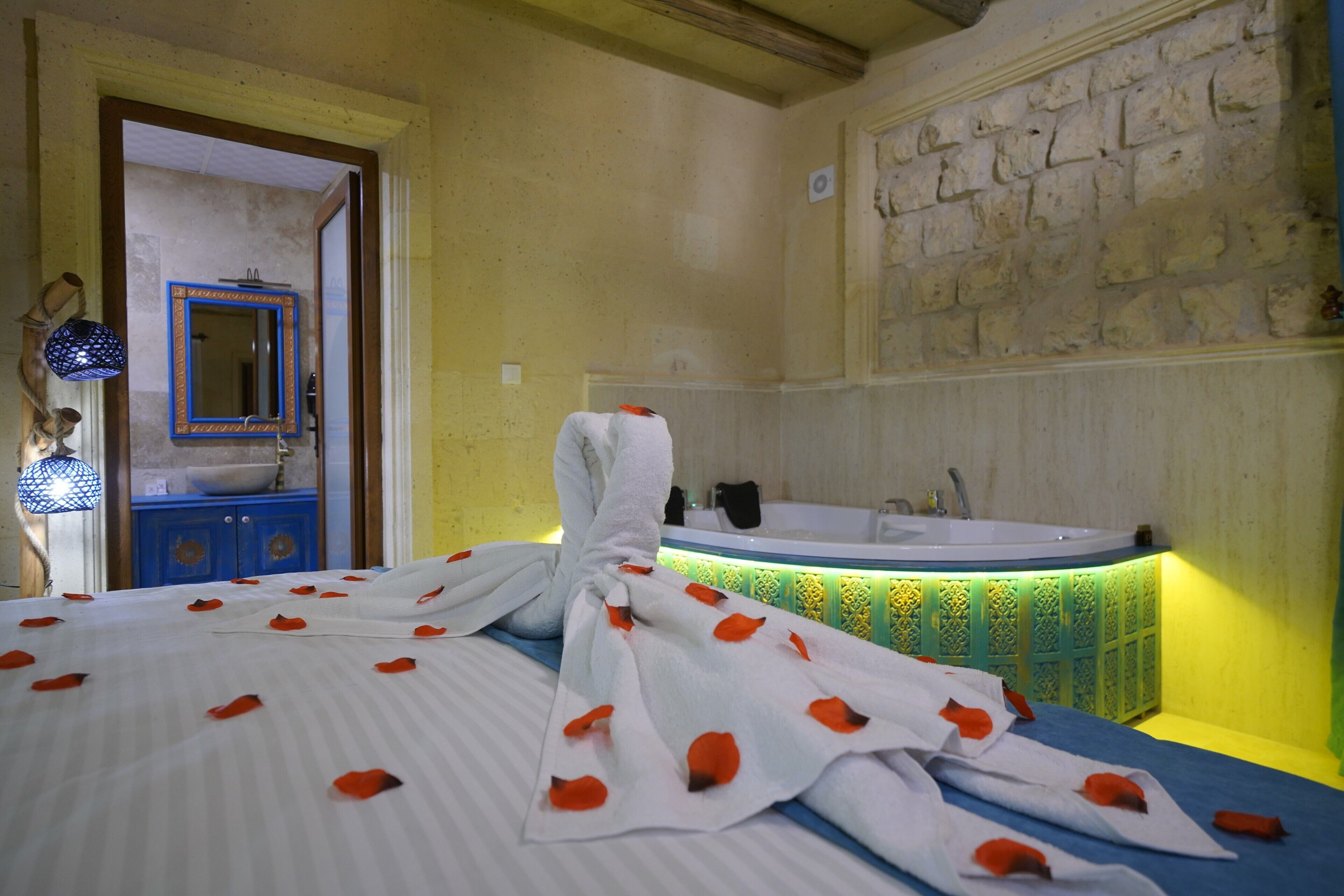 A hotel room with a bed, a bathroom with a bathtub, and a stone wall.