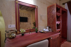 A room with a wooden desk, a mirror, a telephone, a small plant, and a cabinet with decorative carvings.
