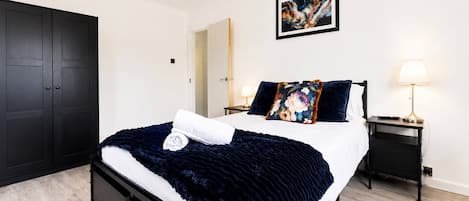 A modern bedroom with a large bed, a wardrobe, a bedside table with a lamp, and a painting on the wall.