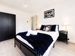 A modern bedroom with a large bed, a wardrobe, a bedside table with a lamp, and a painting on the wall. - Ultra-spacious 2 BR In Central Wimbledon! (London)
