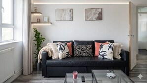 En moderne stue med en sort sofa, et sofabord i glas og en potteplante.