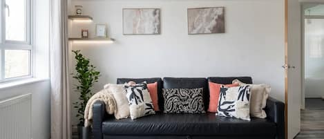 A modern living room with a black sofa, a glass coffee table, and a potted plant.