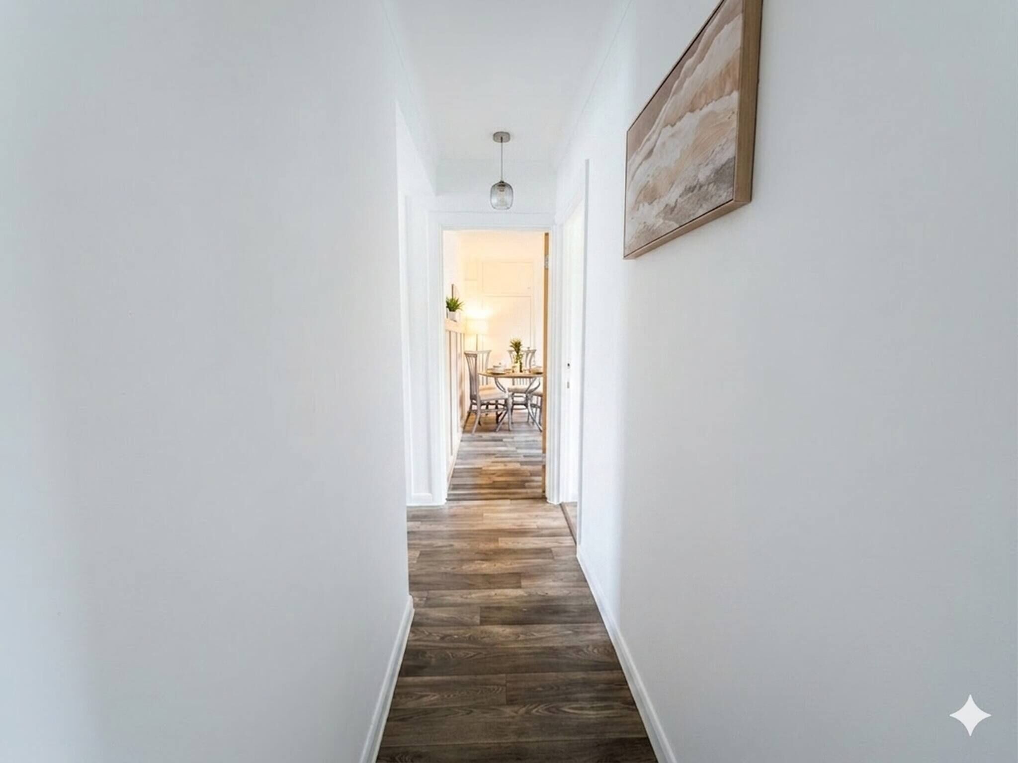 A hallway with a wooden floor leading to a dining area with chairs and a table.