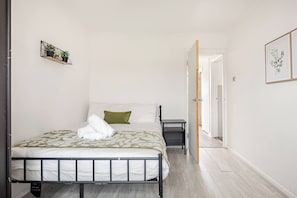 Ein ordentlich eingerichtetes Schlafzimmer mit einem Bett, Nachttisch und einer kleinen Ablage mit Pflanzen.