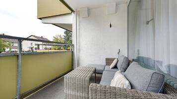 Ein Balkon mit einer Rattan-Couch, Kissen und einem kleinen Tisch.