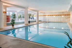 Ein Innenpool mit klarem Wasser, umgeben von weißen Säulen und einer Wand mit einem wellenartigen Muster.