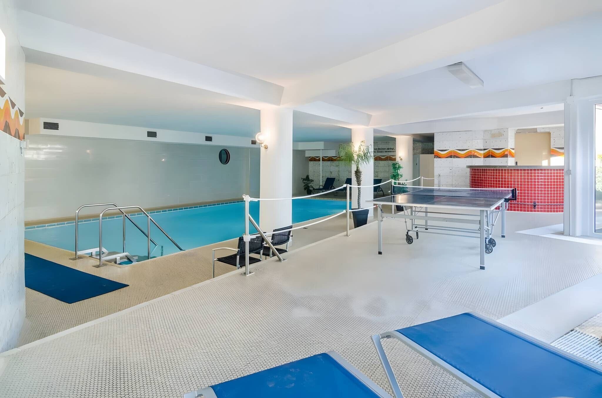 Ein Hallenbad mit Sprungbrett, Liegestühlen und einem Tischtennis-Tisch.