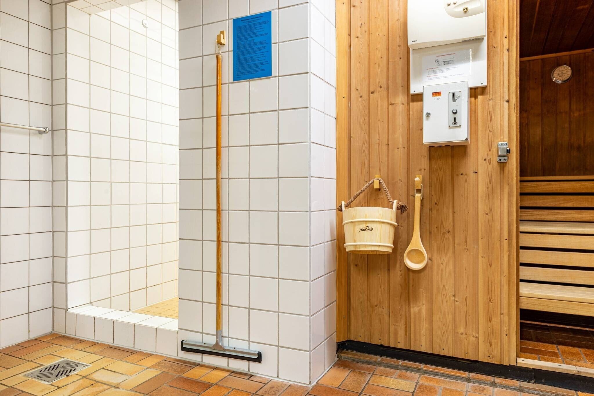Une salle de bain avec des murs carrelés de carreaux blancs, une porte en bois, un espace douche et un sèche-mains.