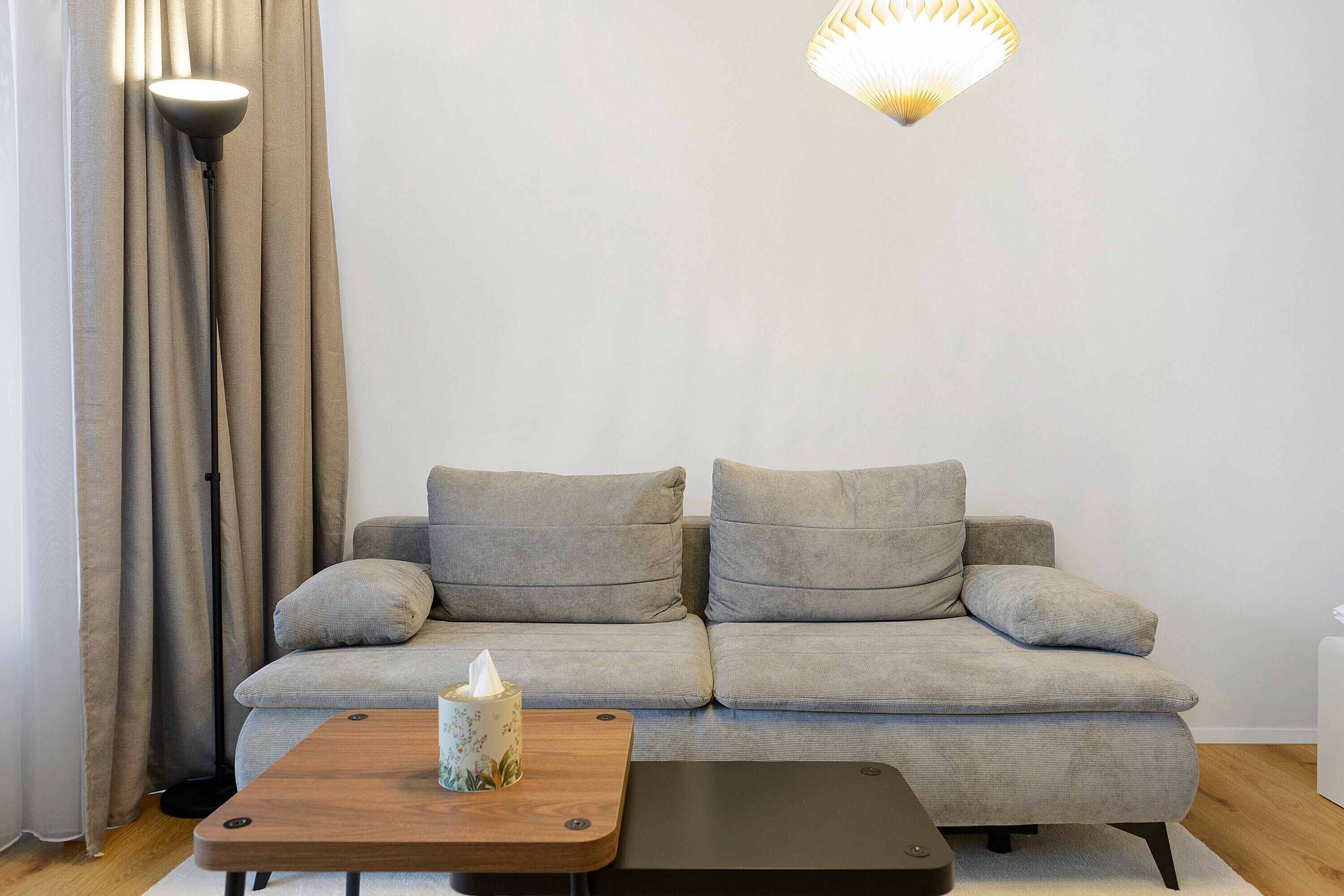Ein Wohnzimmer mit grauem Sofa, einem Holztisch und einer Wandleuchte.