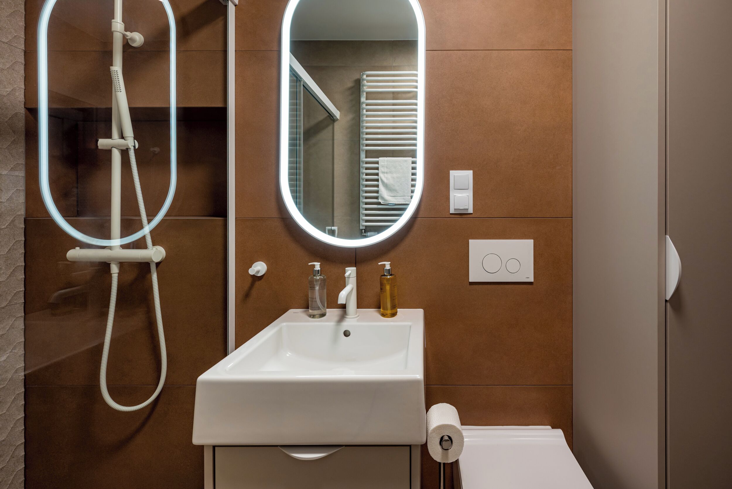A bathroom with a white sink, a handheld showerhead, a mirror, and a towel rack.