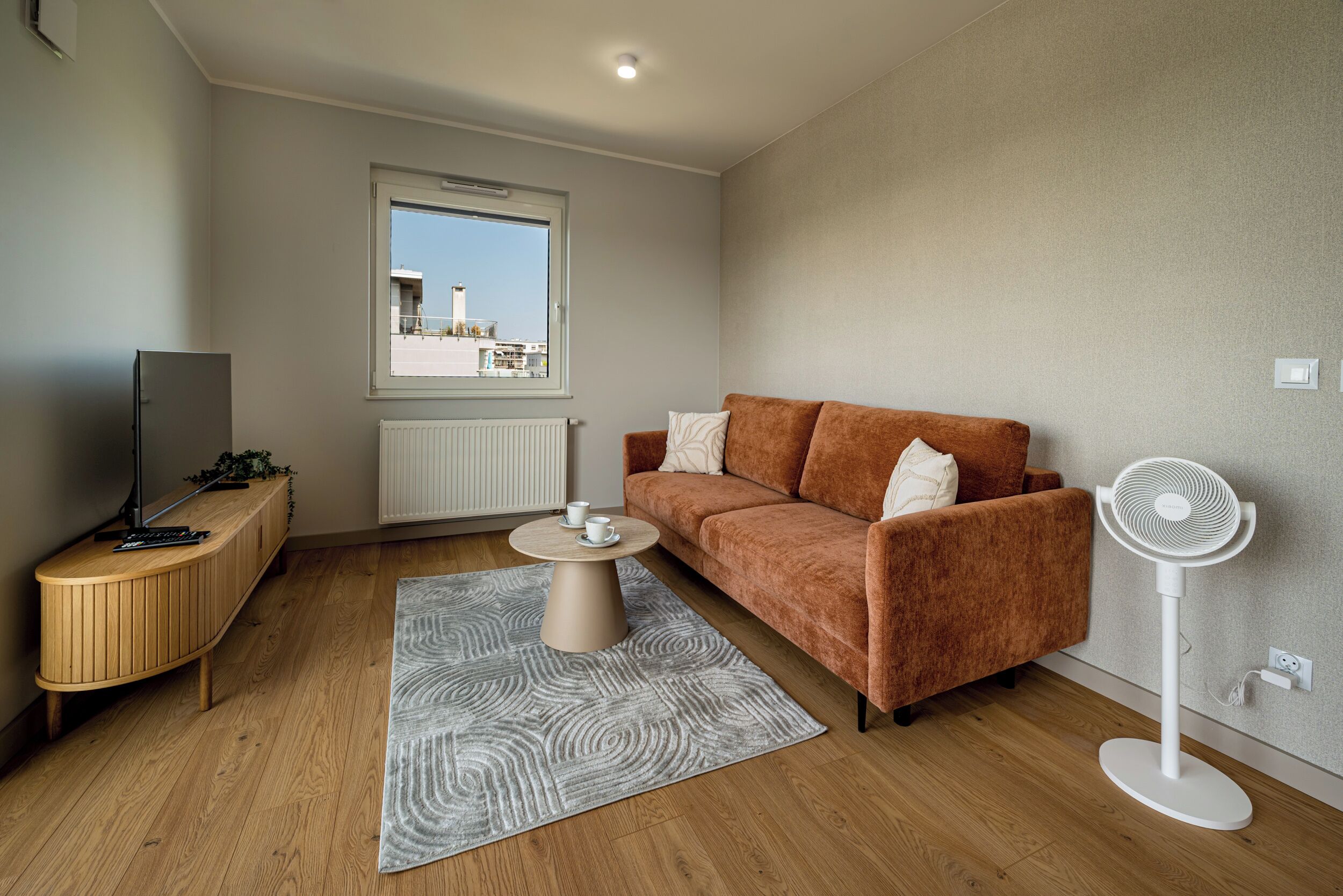 Ein modernes Wohnzimmer mit einer Couch, einem Couchtisch, einem Fernseher und einem Standventilator.