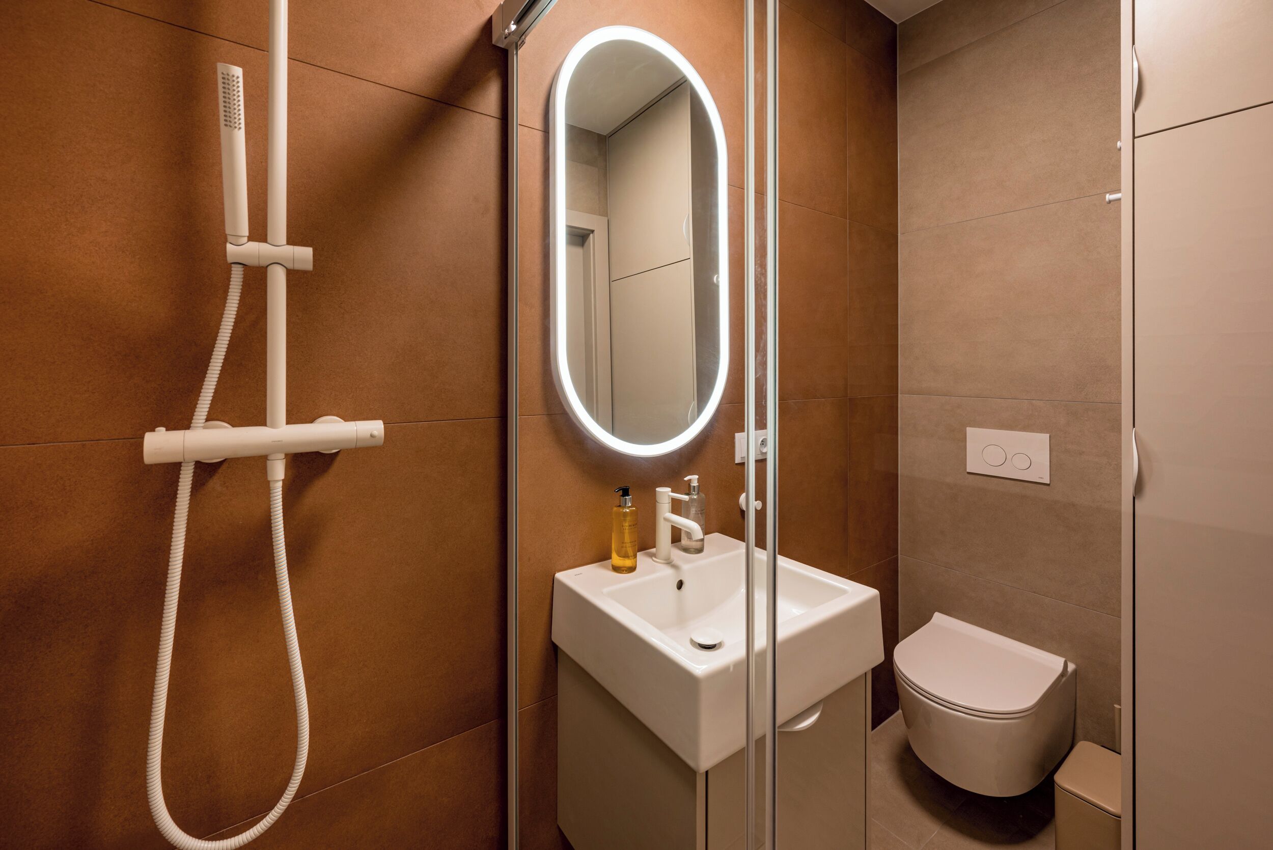 A modern bathroom with a glass-enclosed shower, a white sink, a mirror, and a toilet.