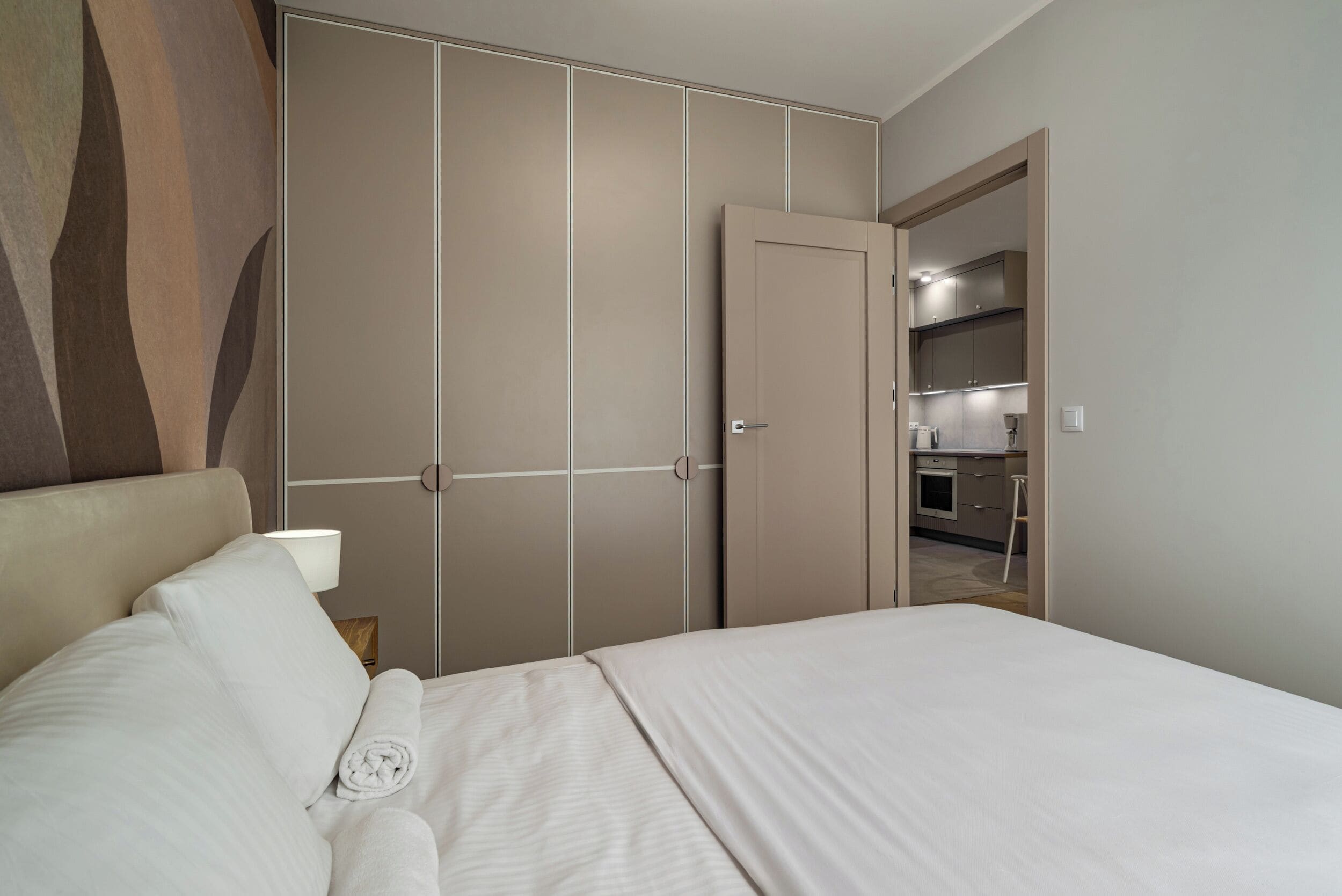 Ein Schlafzimmer mit einem Bett, einem Nachttisch, einer Lampe und einem Kleiderschrank mit Spiegel.