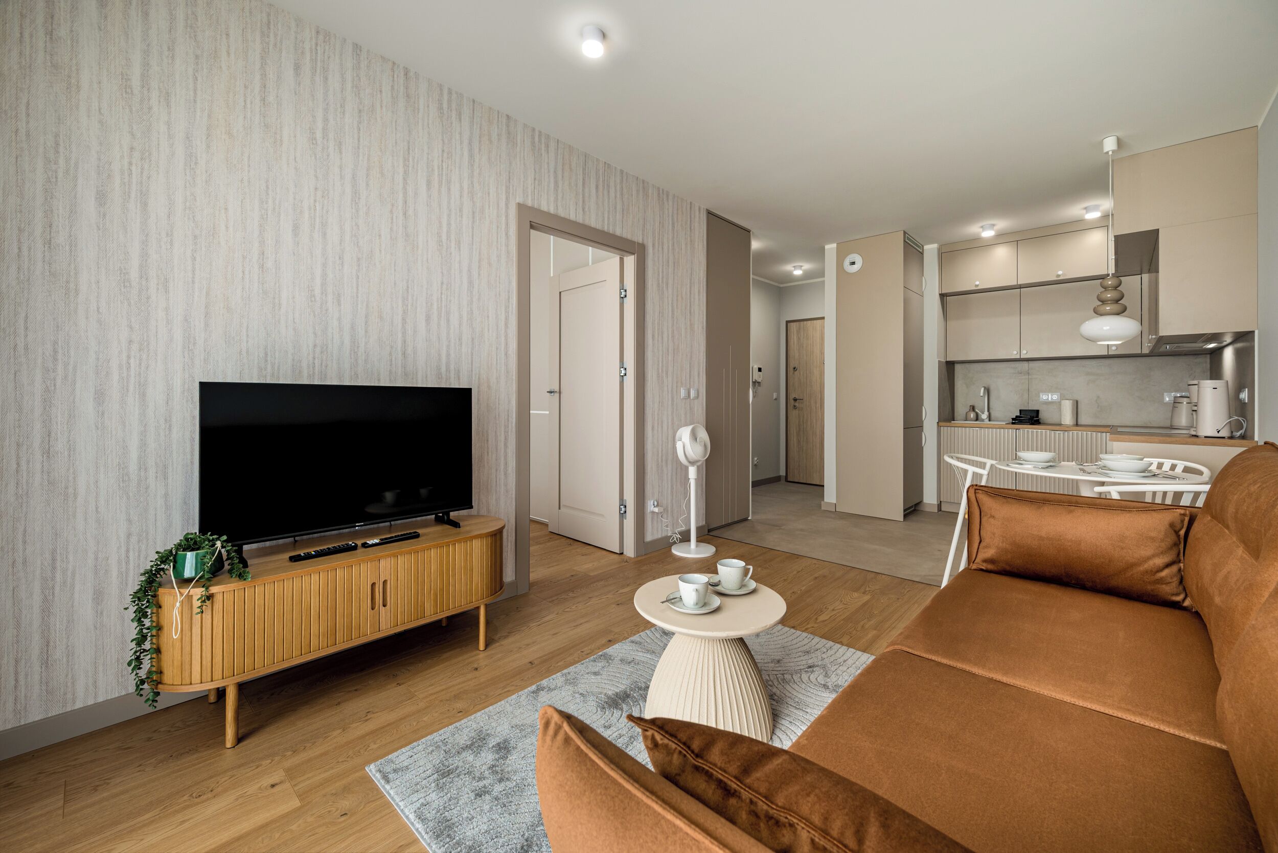 A modern living room with a flat-screen TV, wooden entertainment unit, and a brown sofa.