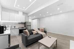 Eine moderne Küche mit weißen Schränken, einem grauen Sofa und einem Holzesstisch.