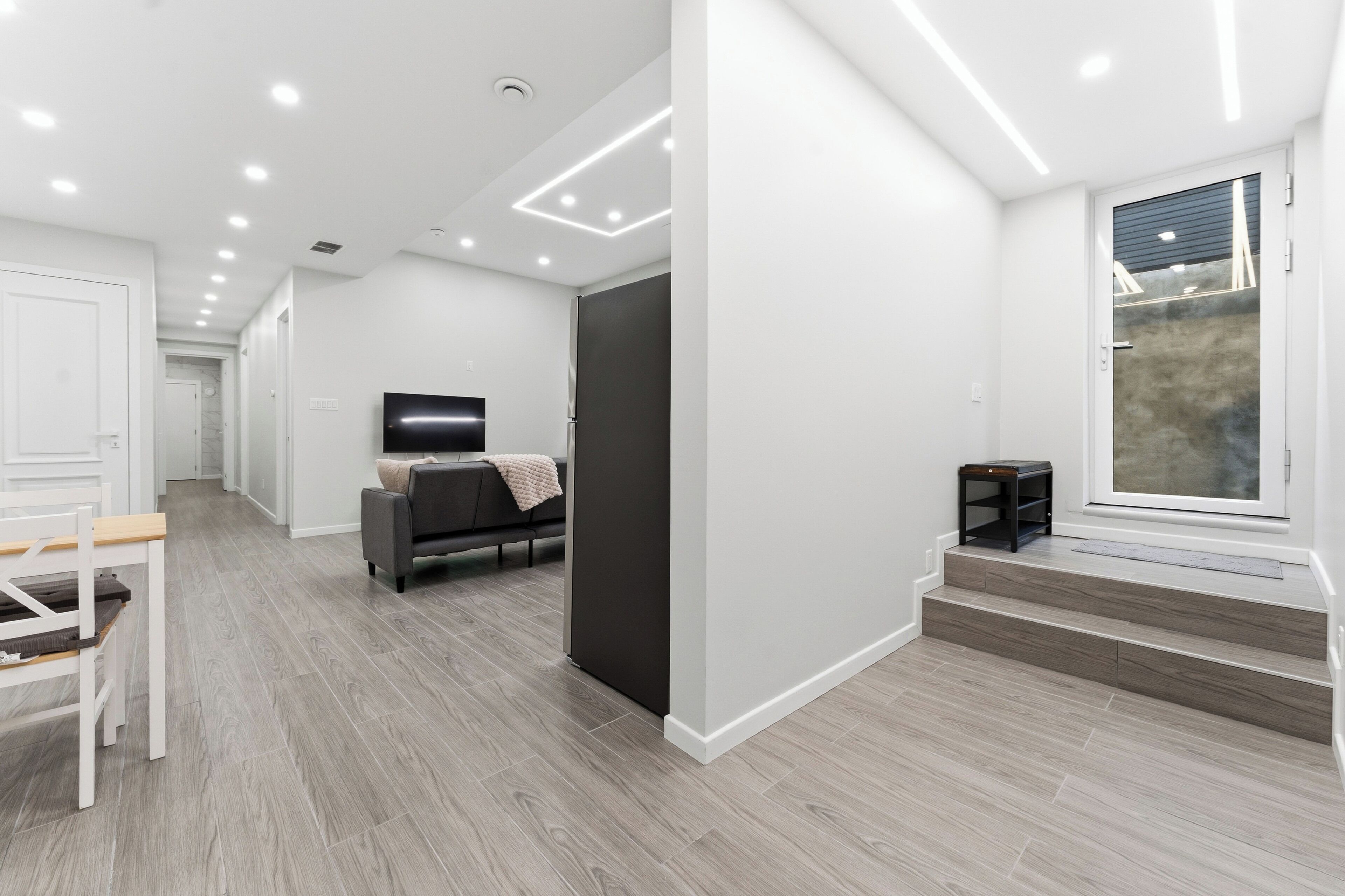 A modern interior with a hallway leading to a living area, a flat-screen TV, and a window with a view.