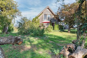 A rustic wooden house with a sloped roof, surrounded by a well-maintained garden with various plants and a large tree in the foreground. - Vacation home 'am quittenbaum', family vacation on Lake Constance (Überlingen)