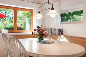 Un coin repas avec une table ronde, des chaises, un vase de fleurs, une bougie et une bibliothèque remplie de livres.