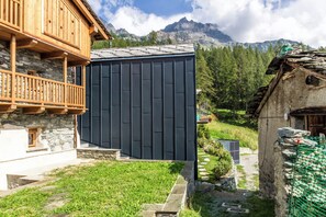 Ein traditionelles Chalet mit Steinaußenwand, Holzbalkon und Blick auf eine Berglandschaft.