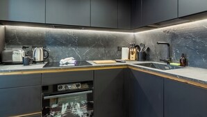 A modern kitchen with dark cabinetry, a marble countertop, and built-in appliances. - Petit Reins - Alpine Lodge close to Ski Return (Valtournenche)