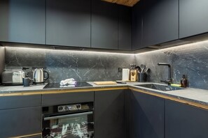 A modern kitchen with dark cabinetry, a marble countertop, and built-in appliances. - Petit Reins - Alpine Lodge close to Ski Return (Valtournenche)