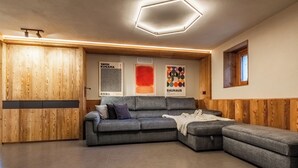 A modern living room with a sectional sofa, wooden panel walls, and artwork on the wall. - Petit Reins - Alpine Lodge close to Ski Return (Valtournenche)