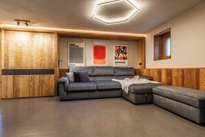 A modern living room with a sectional sofa, wooden panel walls, and artwork on the wall. - Petit Reins - Alpine Lodge close to Ski Return (Valtournenche)
