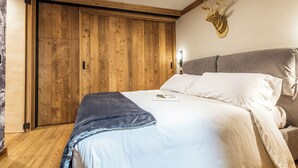 A bedroom with a wooden wardrobe, a bed with white bedding, and a mounted deer head on the wall. - Petit Reins - Alpine Lodge close to Ski Return (Valtournenche)