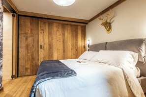 A bedroom with a wooden wardrobe, a bed with white bedding, and a mounted deer head on the wall. - Petit Reins - Alpine Lodge close to Ski Return (Valtournenche)
