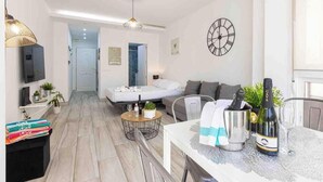 A modern living room with a sofa, a dining table with a bottle of champagne, and a wall clock. - 'El Ciaboga' Apartment with Wi-Fi and Air Conditioning (Torremolinos)