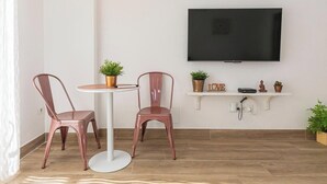 A room with a round table, two chairs, a flat-screen TV mounted on the wall, and a white shelf with decorative items and plants. - 'El Ciaboga' Apartment with Wi-Fi and Air Conditioning (Torremolinos)
